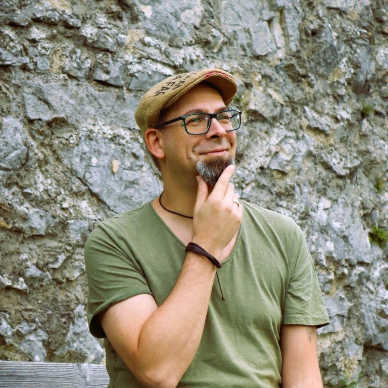 Michael Rohacs Coaching Mann mit Brille und Mütze, nachdenklich vor einer steinernen Wand.