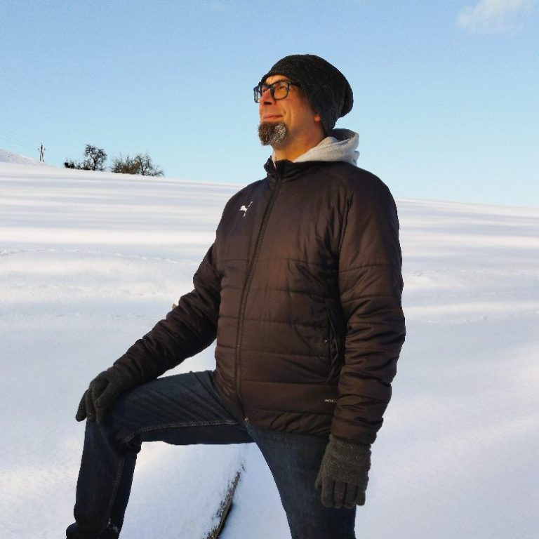 Michael Rohacs Coaching Mann mit Brille und kurzen Haaren, steht lächelnd vor einer grünen Landschaft.